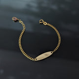 14K gold baby ID bracelet for girls with a blank nameplate and pink gemstone charm, displayed on a black background