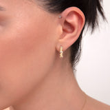 Close-up of woman's ear wearing 14k gold hoop earrings with baguette-cut CZ stones

