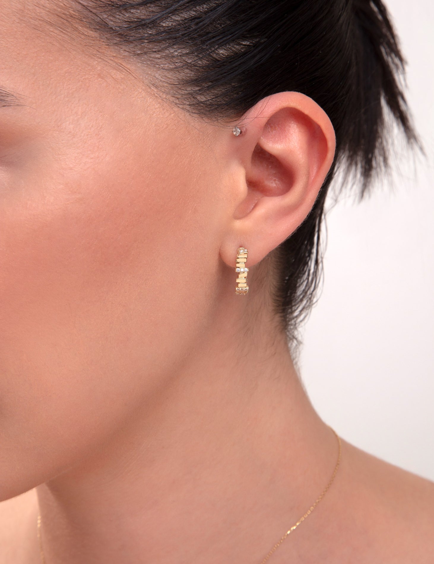 Close-up of woman's ear wearing 14k gold hoop earrings with baguette-cut CZ stones

