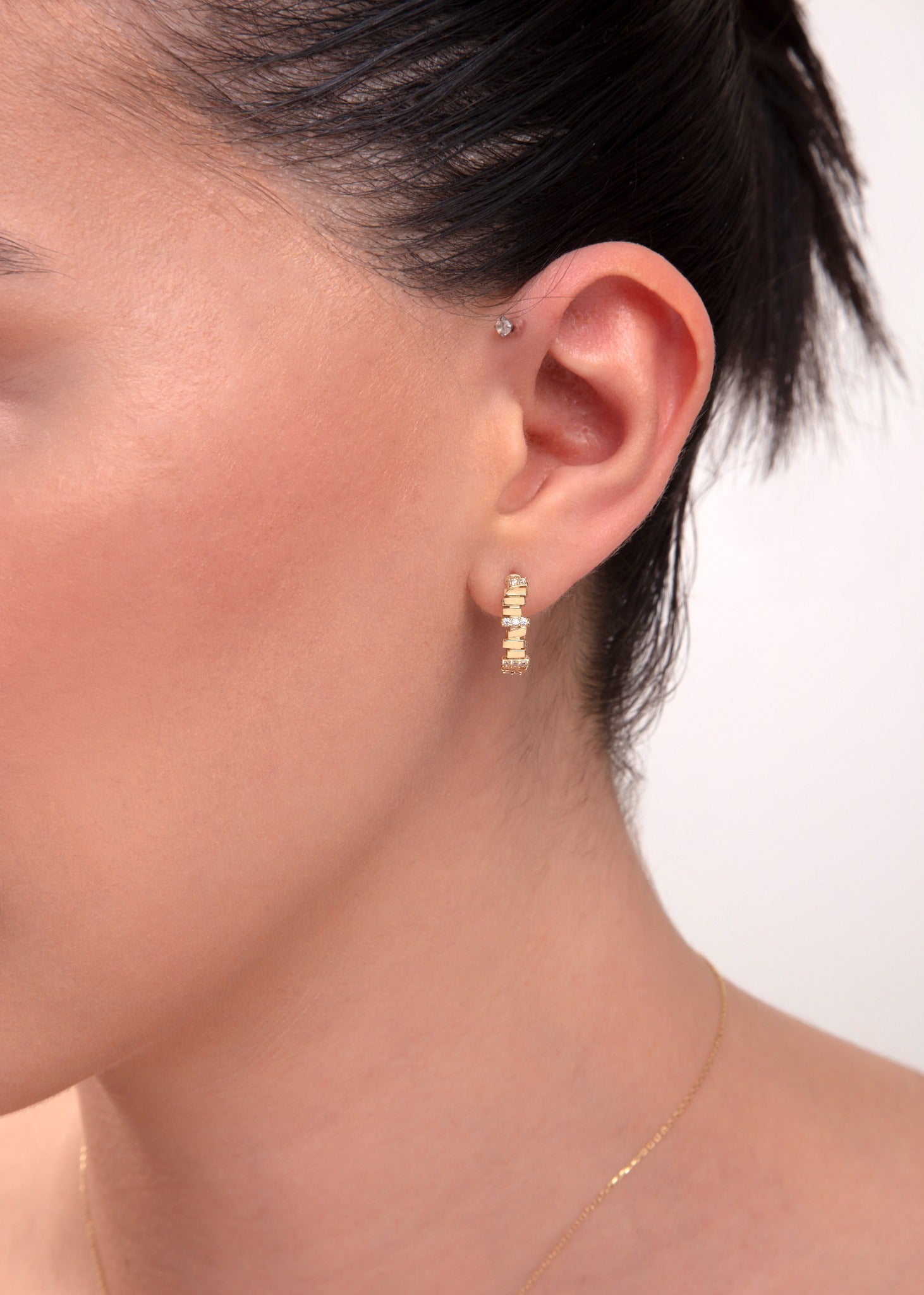 Close-up of woman's ear wearing 14k gold hoop earrings with baguette-cut CZ stones

