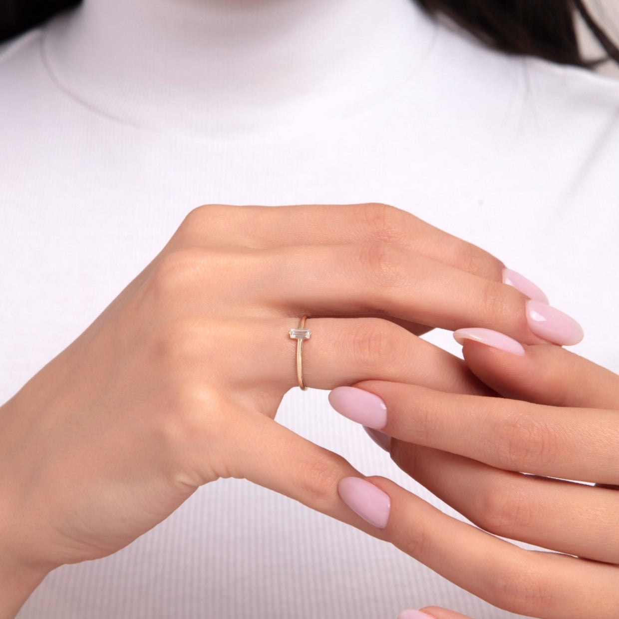 Close-up of a woman's hand wearing a delicate 14K gold ring with a single baguette-cut stone on a thin band