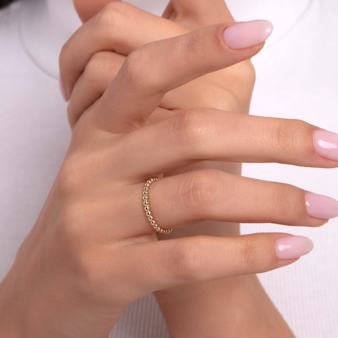 Woman wearing a minimalist 14K gold beaded ring on her finger with light pink nails