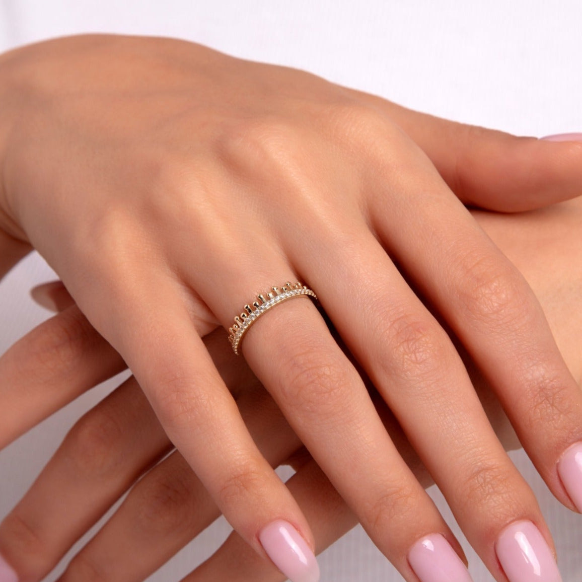 Close-up of a hand wearing a 14K gold eternity ring with beaded crown-style detailing and fine stones