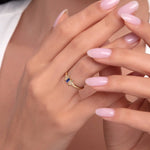 Model wearing a 14K gold ring featuring a baguette-cut blue sapphire and two diamond accents.