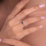 Woman wearing a 14K gold ring with round blue sapphire and delicate diamond side stones