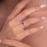 Woman wearing a 14K gold ring with round blue sapphire and delicate diamond side stones