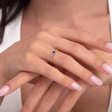 Close-up of a woman's hands wearing a delicate 14K gold blue sapphire solitaire ring with side stones