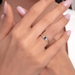 Close-up of a hand wearing a minimalist 14K gold ring with a blue sapphire center stone and two diamond accents.
