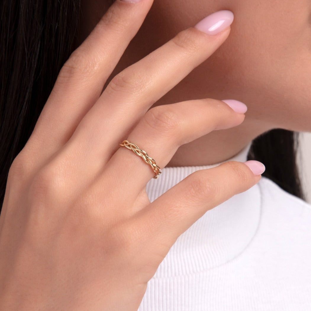 Woman wearing a 14K gold braided rope-style ring on her finger, styled with a white top
