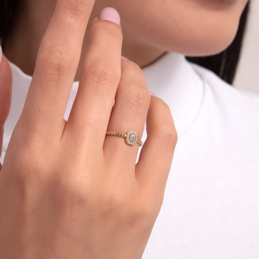 A 14K gold chain-textured ring featuring a cushion-cut center stone surrounded by a halo of smaller diamonds, shown on a hand with soft pink nails.