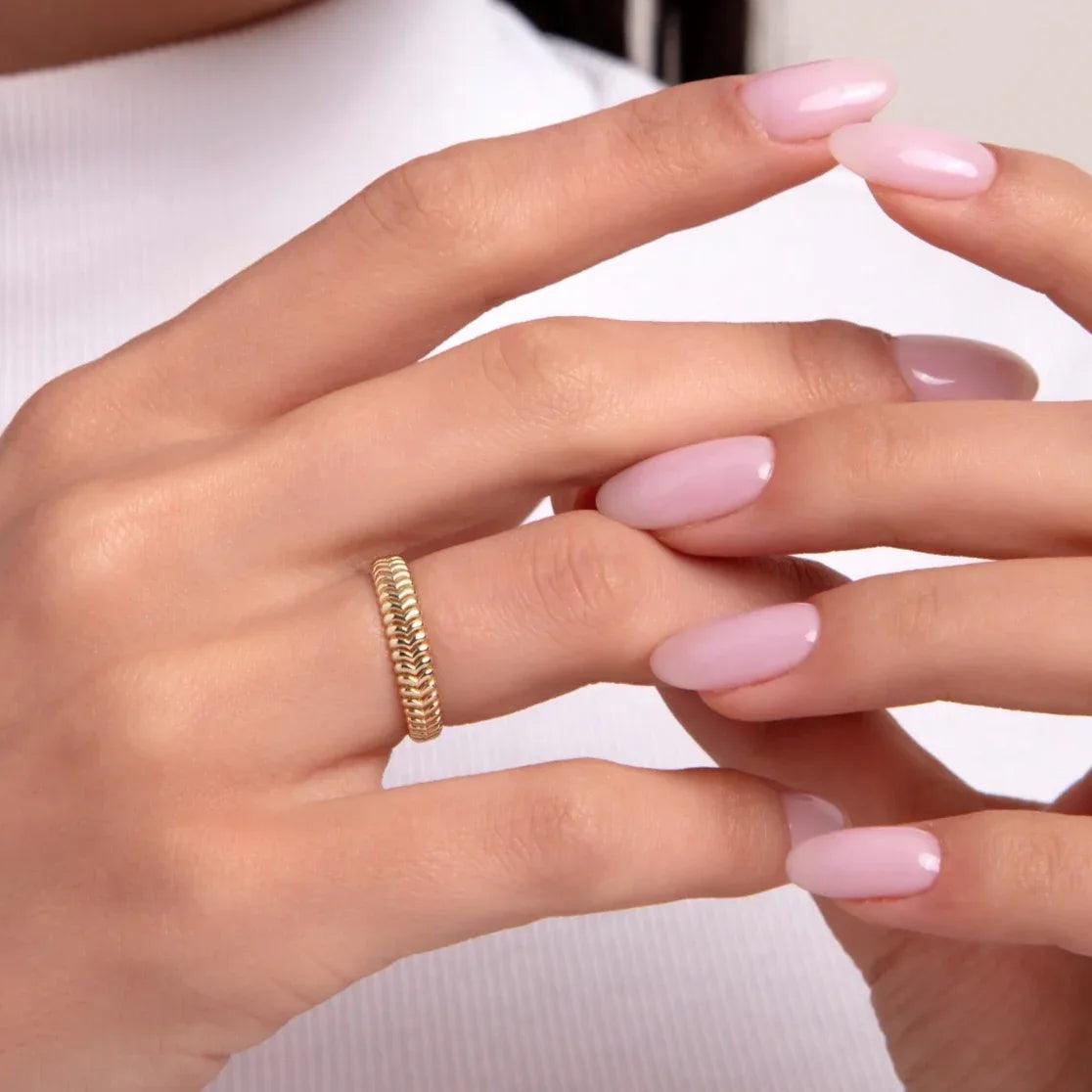 Close-up of a woman's hand wearing a 14K gold ring with a chevron-beaded texture, perfect for stacking