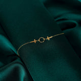 14K gold bracelet with two cross charms and a textured circular centerpiece on deep green fabric.