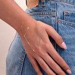 Model wearing a 14k gold hand chain bracelet with multiple cross charms over blue denim pants

