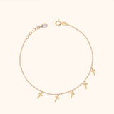 14K gold bracelet with five delicate cross charms on a cream background