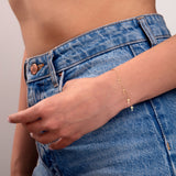 Minimal 14k gold cross charm bracelet worn on wrist with high-waisted blue jeans and white knit top

