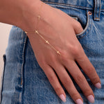 Close-up of a woman wearing a 14k gold hand chain bracelet with cross charms, styled with blue jeans

