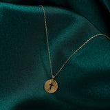 Minimalist 14K gold medallion necklace with a central cutout cross and radiant sunbeam engravings, styled on emerald green satin.