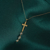 Minimal 14K gold cross necklace with crystal drop accents photographed on emerald green silk background