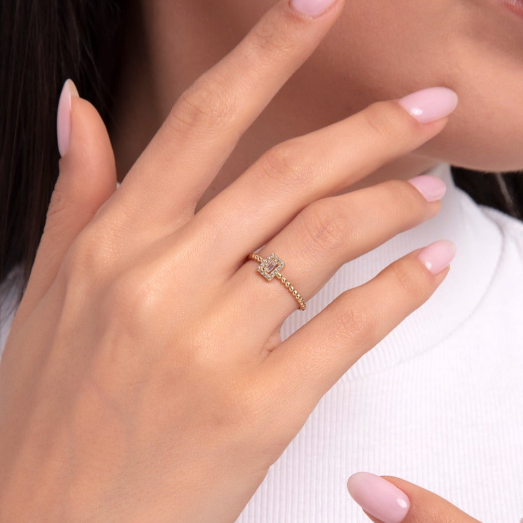 Woman wearing a delicate 14K gold ring with a diamond-studded cross and beaded band