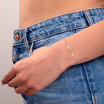 Elegant 14k gold bracelet with cross and circle charms on a model’s wrist wearing blue jeans

