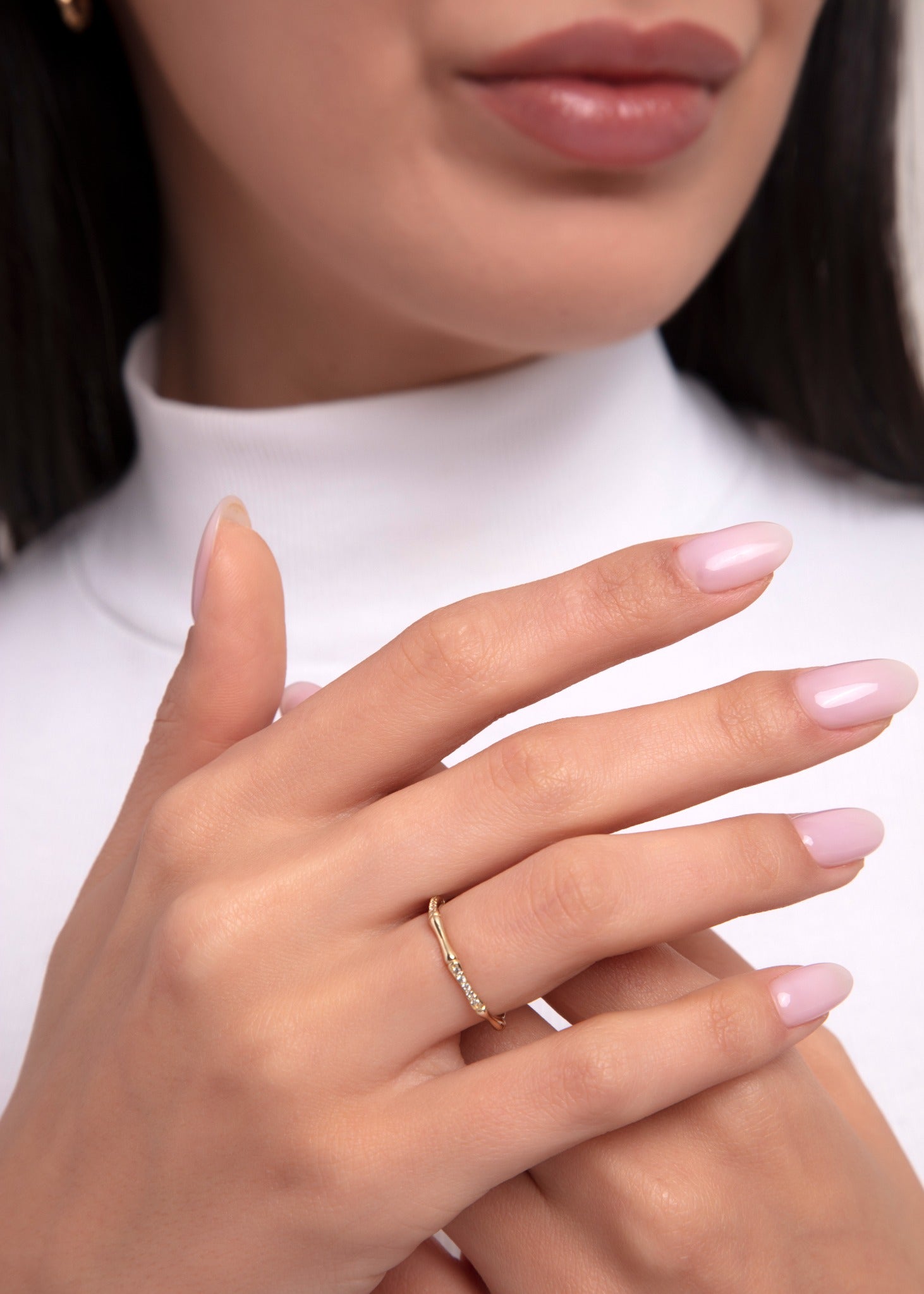 Close-up of a woman wearing a dainty 14K gold ring with a gentle wave shape and small diamond accents