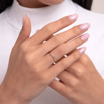 A dainty 14K gold ring with a gentle curve, accented by small diamonds, shown on a hand with soft pink nails in an elegant pose.