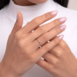 A dainty 14K gold ring with a gentle curve, accented by small diamonds, shown on a hand with soft pink nails in an elegant pose.