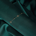 14K gold bracelet featuring three dainty flower charms and bead accents, styled on emerald satin fabric