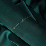 14K gold bracelet featuring three dainty flower charms and bead accents, styled on emerald satin fabric