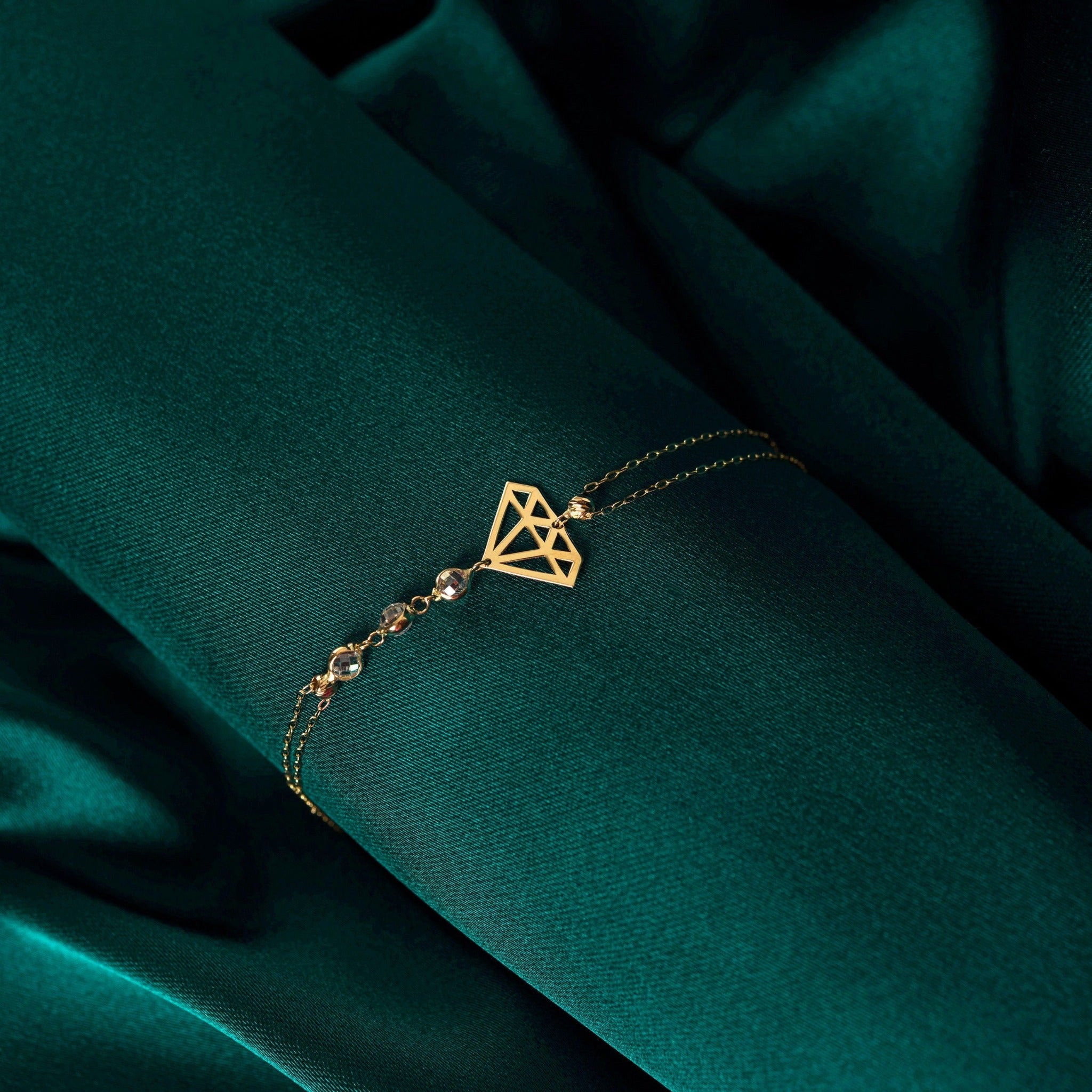 14K gold bracelet with geometric diamond outline and faceted gemstone bead accents on green silk background