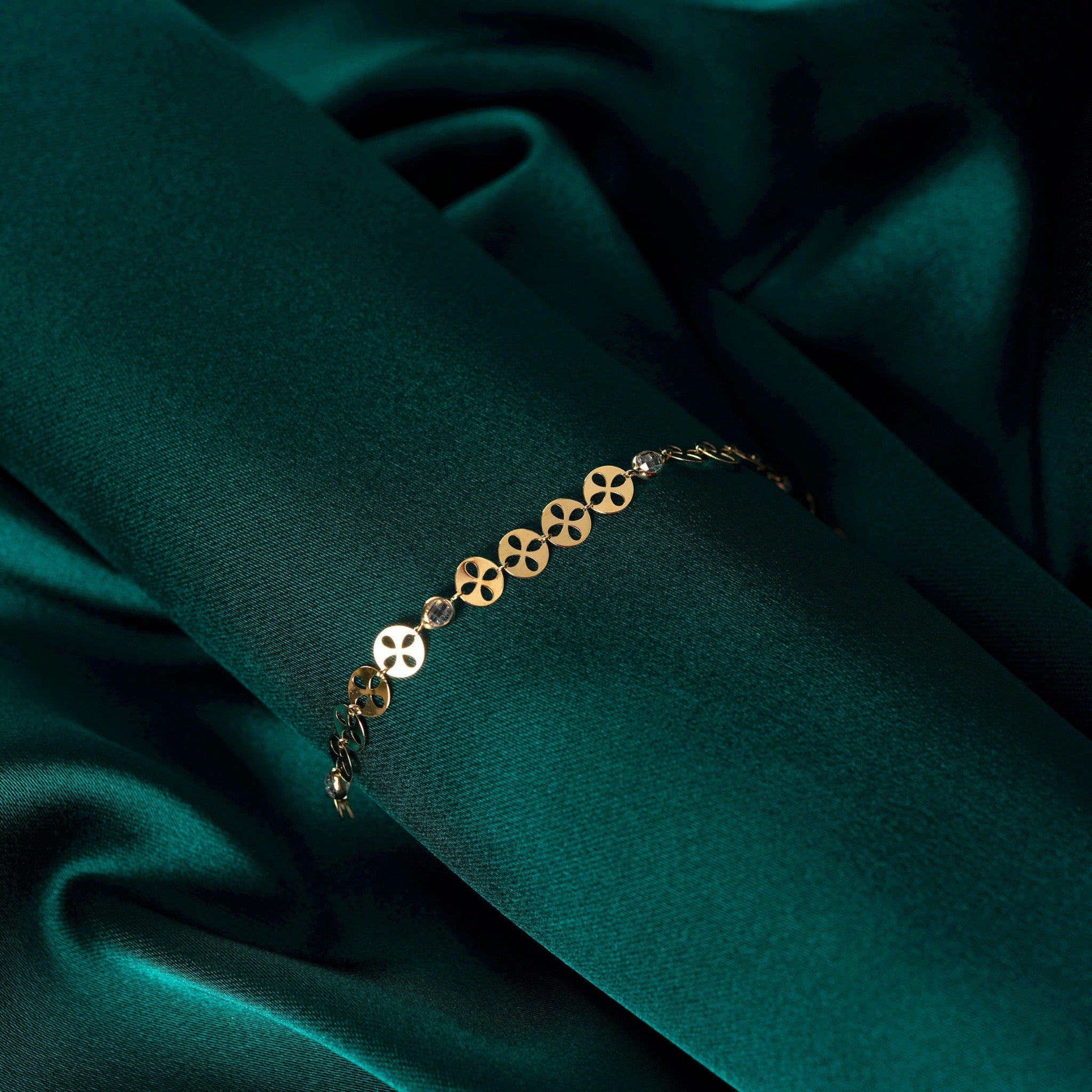 14K gold bracelet with circular disc charms and crystal beads displayed on deep green satin fabric.