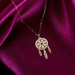 Delicate 14K gold dreamcatcher necklace with intricate circular web and three gold feather charms, displayed on deep pink satin fabric.