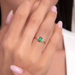 Close-up of a woman wearing a 14K gold ring with a green emerald-cut gemstone and small diamond accents.
