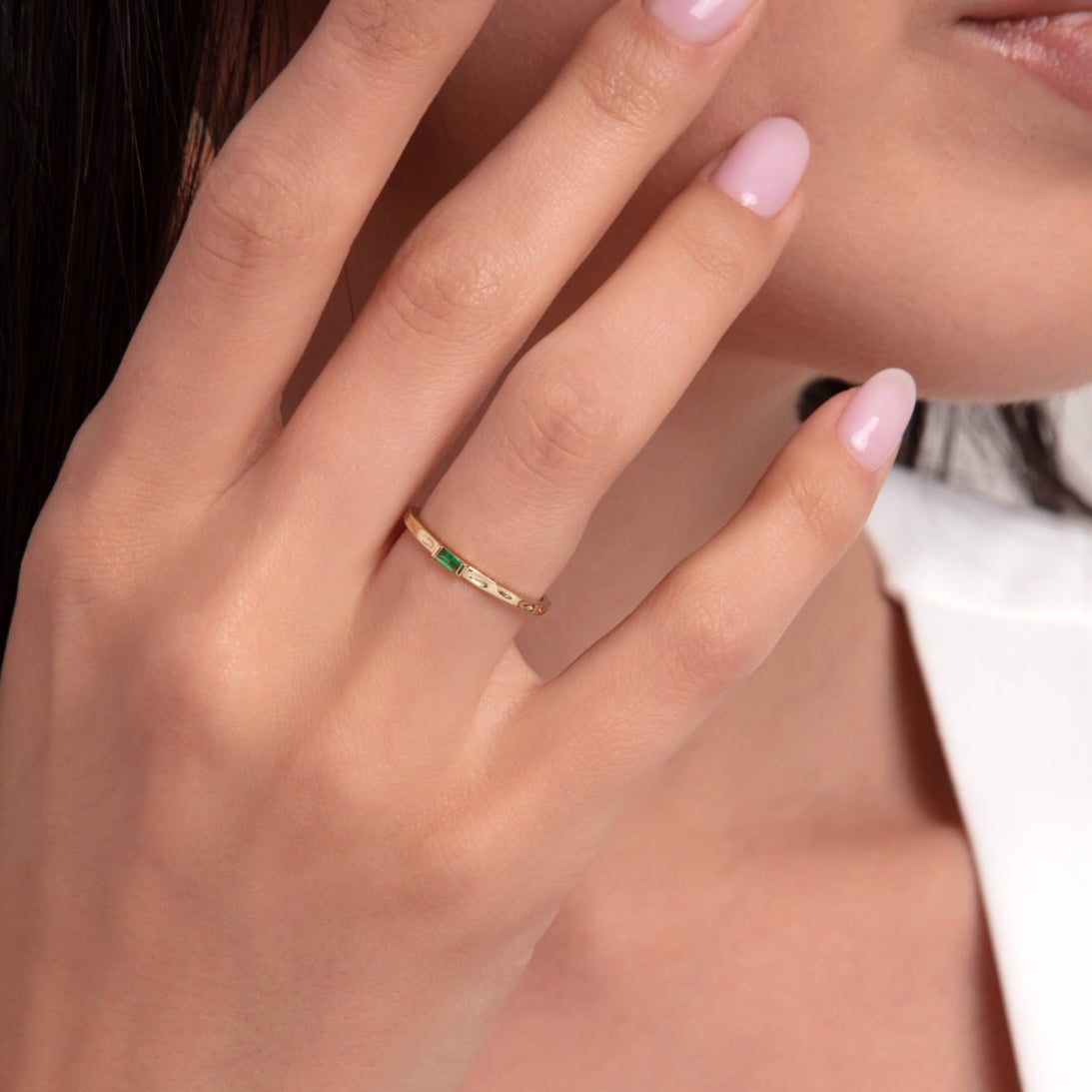 Close-up of a 14K gold ring with a slim emerald bar on a woman's finger