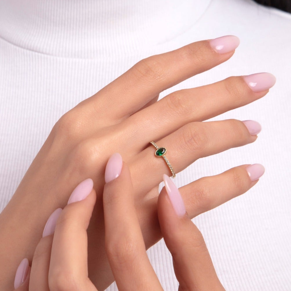 Close-up of a woman's hand wearing a delicate 14K gold ring with an oval-cut green emerald centerpiece