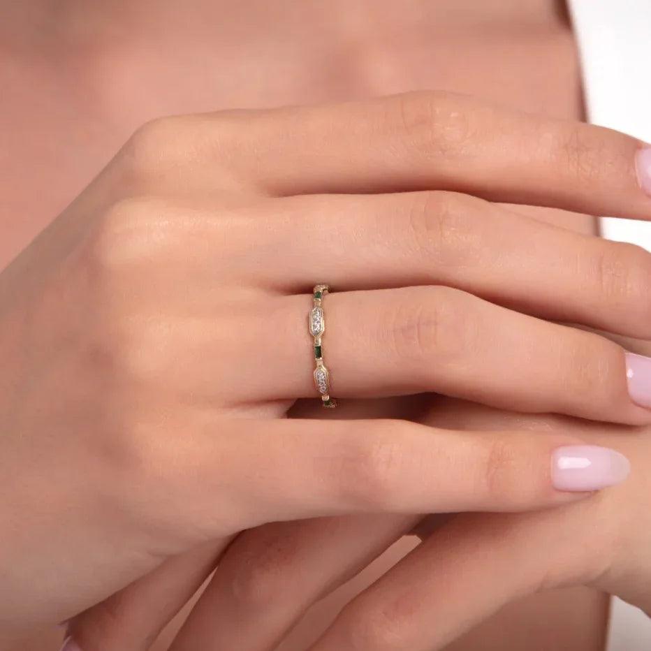 Woman wearing a delicate 14K gold ring with alternating emerald and marquise-cut diamond stones.