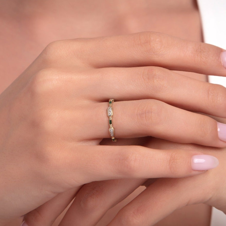 Woman wearing a delicate 14K gold ring with alternating emerald and marquise-cut diamond stones.