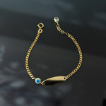 14K gold baby bracelet with evil eye charm and blank ID plate on a black background, designed for protection and customization