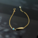 14K gold baby bracelet with evil eye charm and blank ID plate on a black background, designed for protection and customization
