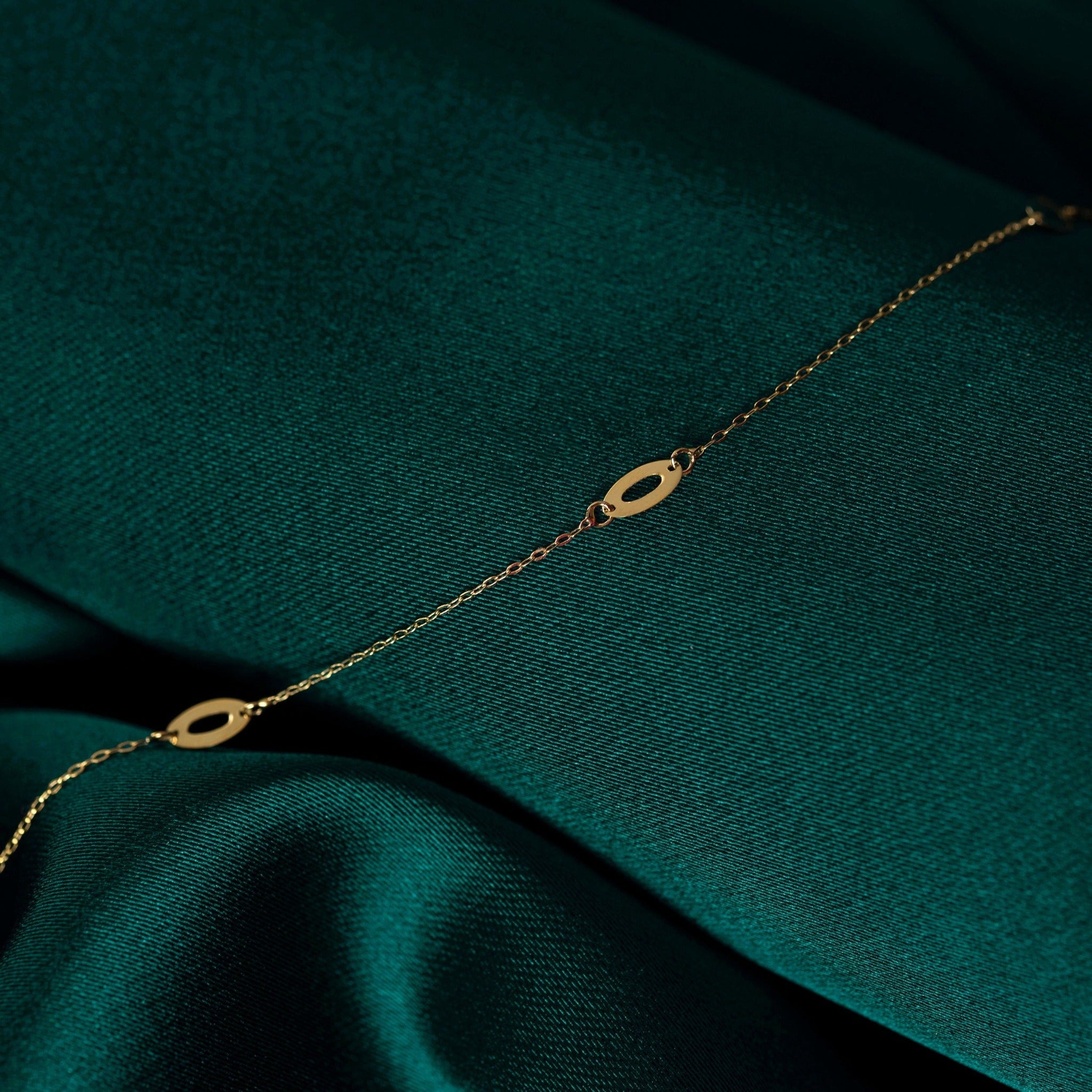 14K gold bracelet with elongated marquise-shaped link elements, displayed elegantly on green satin background.