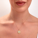 Woman wearing a 14k gold medallion necklace featuring a blue enamel evil eye pendant

