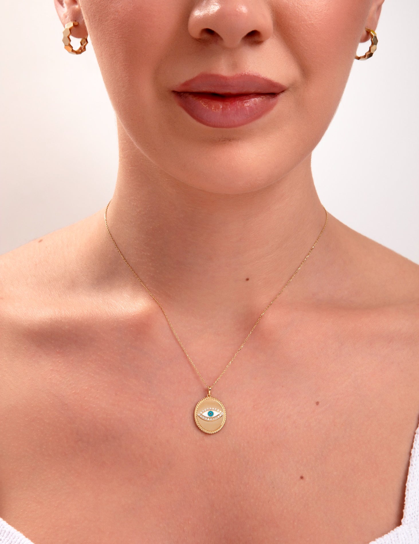 Woman wearing a 14k gold medallion necklace featuring a blue enamel evil eye pendant

