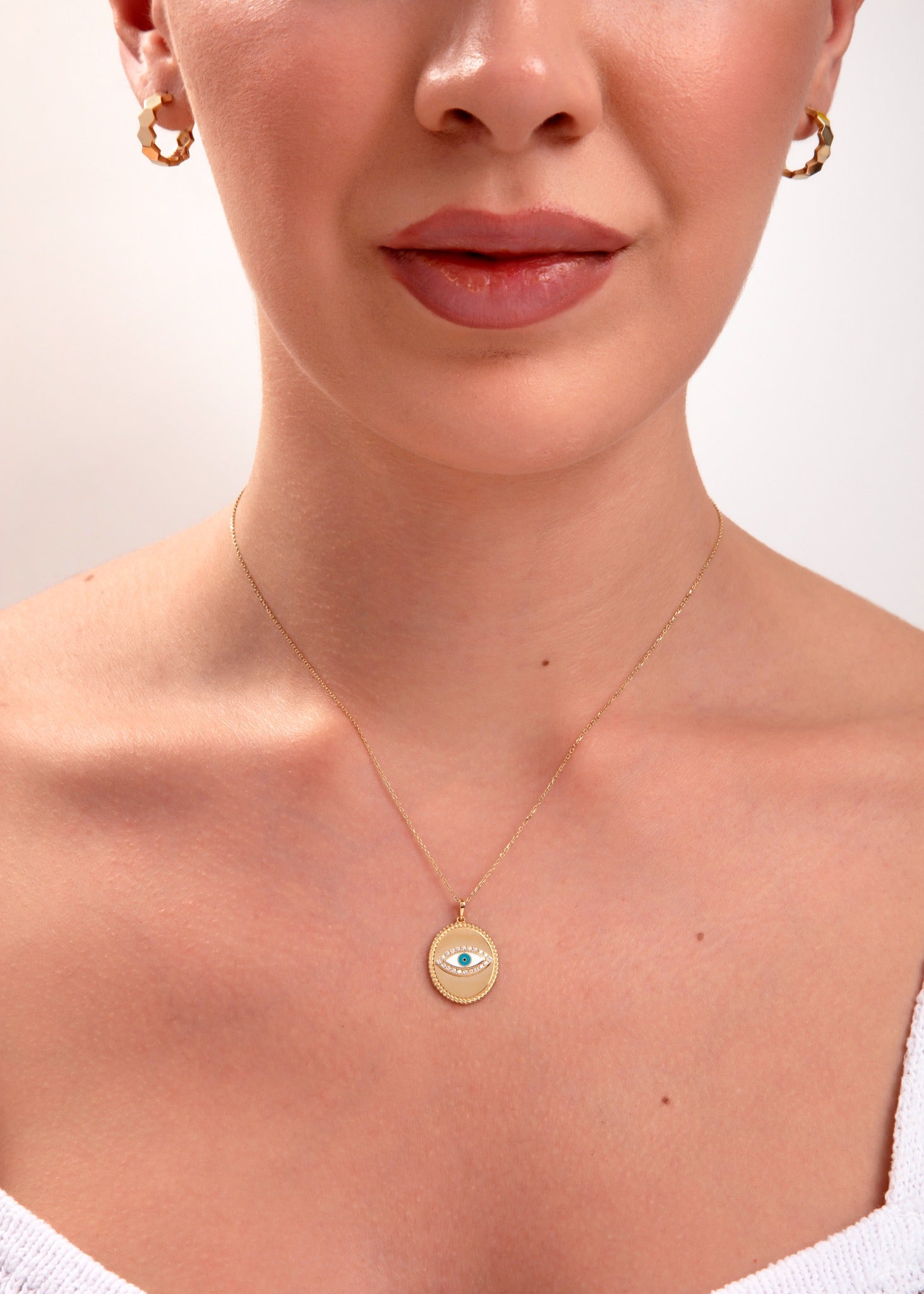 Woman wearing a 14k gold medallion necklace featuring a blue enamel evil eye pendant

