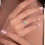 Close-up of a woman's hand wearing a 14K gold evil eye ring with a blue enamel charm