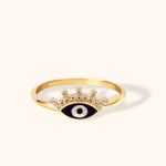 14K gold evil eye ring with crown-shaped CZ stones and navy enamel on light background.