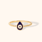 14K gold beaded ring with navy blue enamel evil eye charm in teardrop shape on light background.