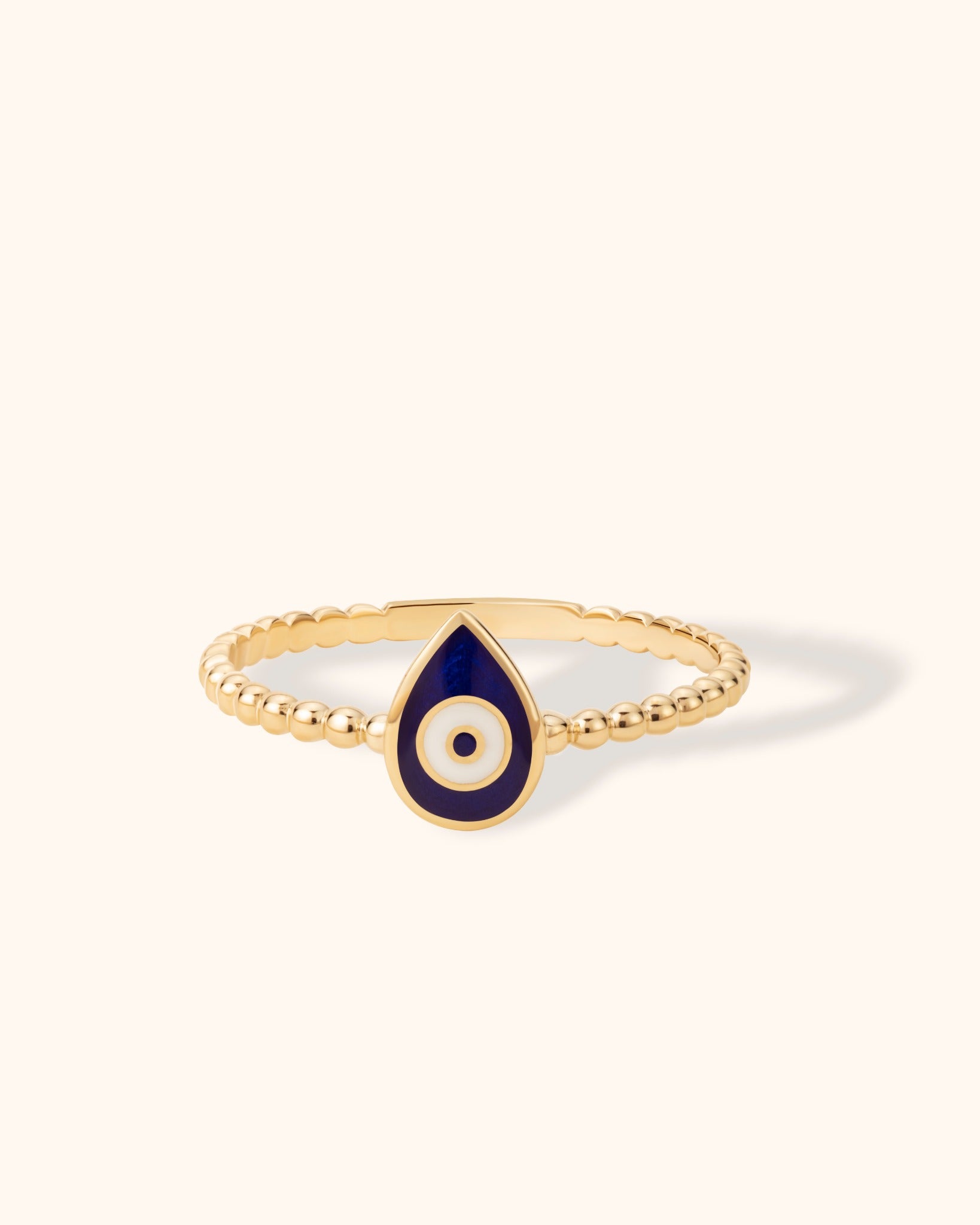 14K gold beaded ring with navy blue enamel evil eye charm in teardrop shape on light background.