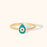 14K gold beaded ring with turquoise enamel teardrop evil eye charm on cream background.