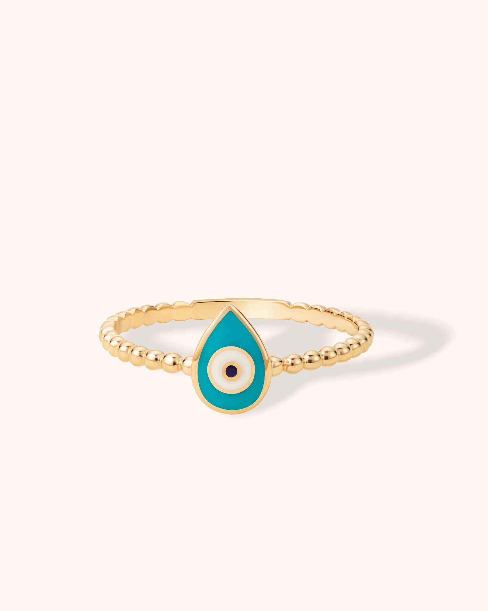 14K gold beaded ring with turquoise enamel teardrop evil eye charm on cream background.