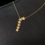 Seven-star cascade necklace in 14K gold displayed on black textured leather background, featuring minimalist celestial design.